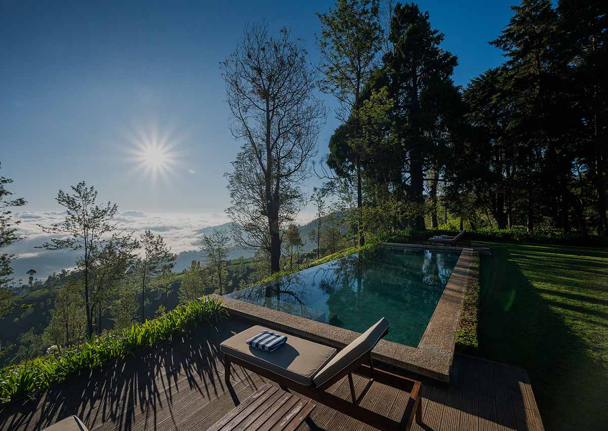 Sun loungers on a timber deck beside the infinity pool, with pines and cloud-filled valleys beyond