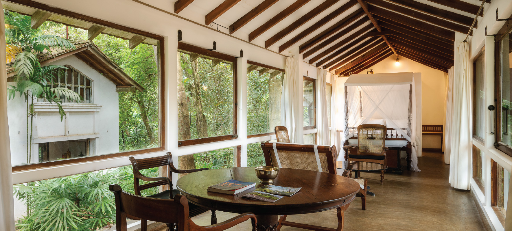 The Glass House, a room walled in glass looking into the tree canopy, a bed and a round table
