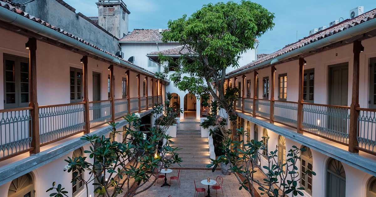 Fort Bazaar, a luxury boutique hotel in Galle, Sri Lanka. Image shows an open-air courtyard in a Portuguese-colonial style building with a large tree and some tables and chairs
